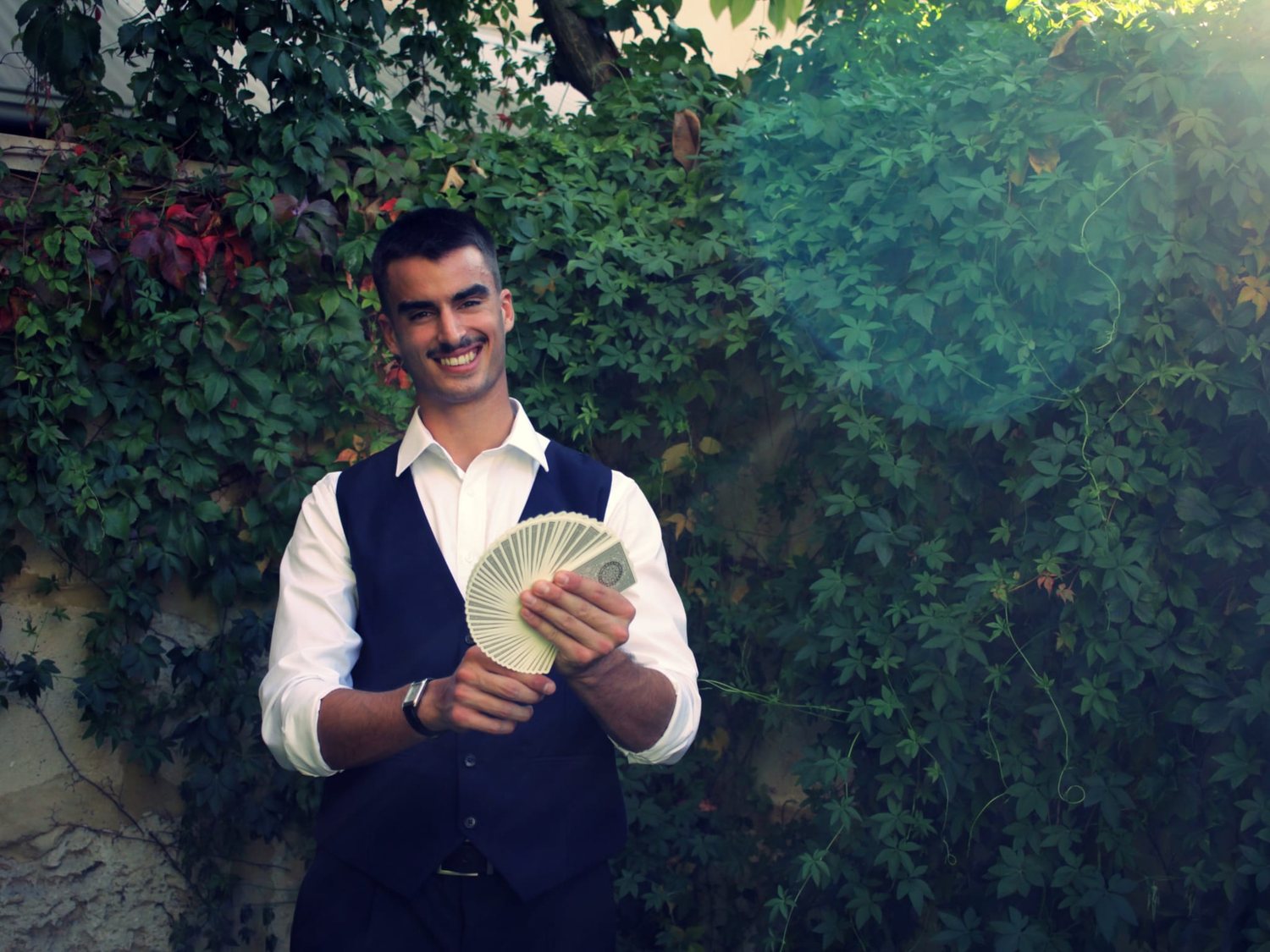 Dominic Miles fanning a full deck of cards in front of ivy